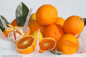 primo piano di arance e limoni intere e affettati su neve bianca e foglie di alloro primo piano