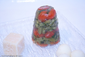 vista da lato di aspic di verdure a forma di cono con fagiolini e peperoni visibili attraverso la gelatina di piatto e sfondo bianco con quadratino di formaggio parmigiano