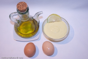 vista dall'alto di un'ampolla con olio di oliva due uova una ciotola di vetro cion maionese e una fetta di limone su sfondo bianco