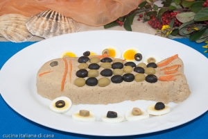 primo piano di forma di pesce fatta con impasto di tonno e patate su piatto ovale bianco con sfondo di conchiglie fiori e bacche