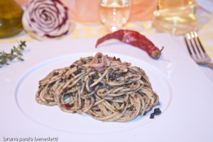 veduta laterale di piatto bianco con spaghetti alla puttanesca con guarnizione di peperoncino cruscio rosso e bicchiere di vuno bianco