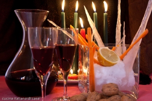 primo piano di noci neve e stalattiti di ghiaccio accanto a bicchieri e caraffa di vino rosso con candele accese sullo sfondo e luce soffusa
