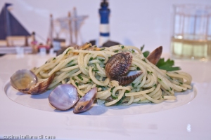 veduta laterale di piatto di spaghetti alle vongole con gusci di vongole e ambientazione marina